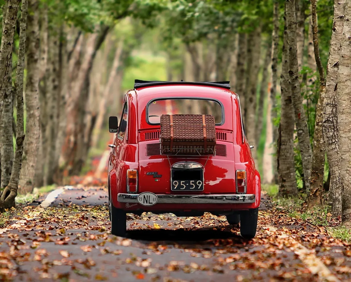 Zabytkowy Fiat 500 zaparkowany w otoczeniu drzew przed budynkiem urzędu.